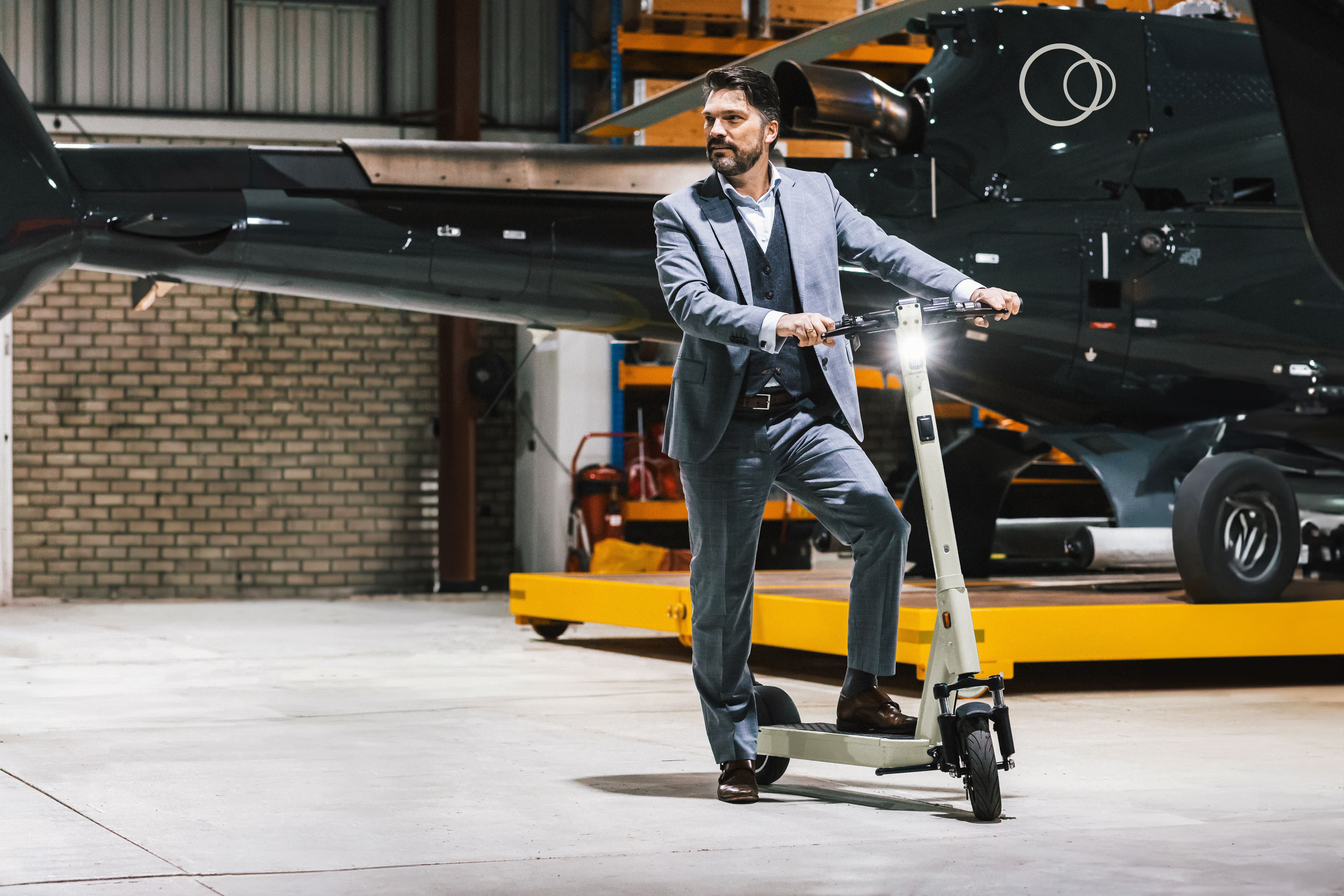 Man in a suit with a SELANA Alpha in a hangar next to a helicopter
